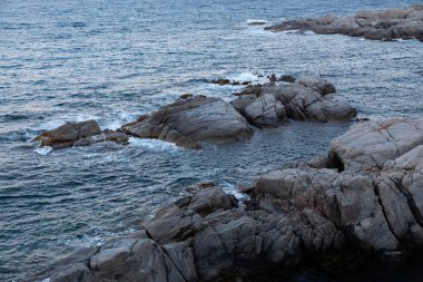 Turkuaz deniz suyu, arka planda tekneler olan kumlu bir sahilde kırılıyor.
