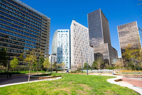 Güneşli bir günde çevresi yeşil ağaçlar ve çimlerle çevrili modern ofis binalarıyla dolu bir iş bölgesi.