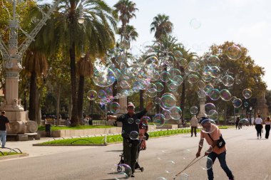 Barselona 'da bir parkta dev sabun köpükleri yapan bir sokak şarkıcısını izleyen turistler