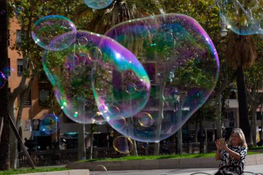 Barselona 'da bir parkta dev sabun köpükleri yapan bir sokak şarkıcısını izleyen turistler