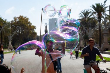 Barselona 'da bir parkta dev sabun köpükleri yapan bir sokak şarkıcısını izleyen turistler