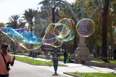 Barselona 'da bir parkta dev sabun köpükleri yapan bir sokak şarkıcısını izleyen turistler