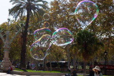 Barselona 'da bir parkta dev sabun köpükleri yapan bir sokak şarkıcısını izleyen turistler