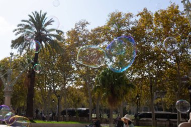 Barselona 'da bir parkta dev sabun köpükleri yapan bir sokak şarkıcısını izleyen turistler