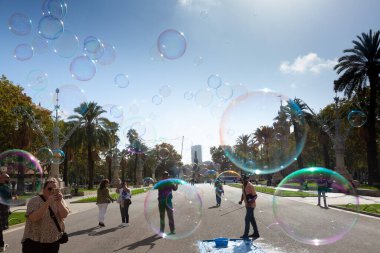 Barselona 'da bir parkta dev sabun köpükleri yapan bir sokak şarkıcısını izleyen turistler