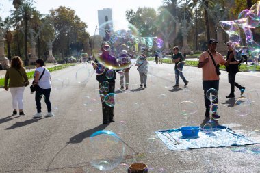 Barselona 'da bir parkta dev sabun köpükleri yapan bir sokak şarkıcısını izleyen turistler