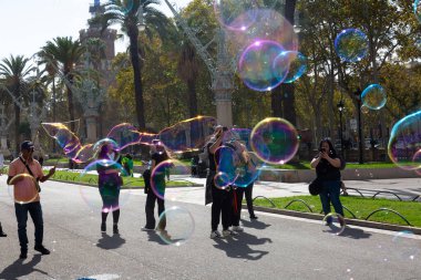Barselona 'da bir parkta dev sabun köpükleri yapan bir sokak şarkıcısını izleyen turistler