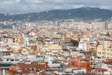 Barselona 'da modern bir binanın üzerinde yükselen üç sanayi bacası bulutlu bir gökyüzünün altında panoramik şehir manzarası sunuyor.