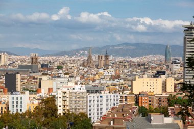 Barselona 'da modern bir binanın üzerinde yükselen üç sanayi bacası bulutlu bir gökyüzünün altında panoramik şehir manzarası sunuyor.