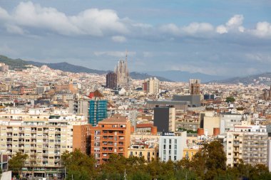 Barselona 'da modern bir binanın üzerinde yükselen üç sanayi bacası bulutlu bir gökyüzünün altında panoramik şehir manzarası sunuyor.