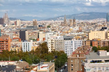 Barselona 'da modern bir binanın üzerinde yükselen üç sanayi bacası bulutlu bir gökyüzünün altında panoramik şehir manzarası sunuyor.