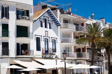 Teslimatçı, güneşli bir günde, İspanya 'da mavi renkli evlerin olduğu dar bir sokakta scooter sürüyor.