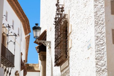 Teslimatçı, güneşli bir günde, İspanya 'da mavi renkli evlerin olduğu dar bir sokakta scooter sürüyor.