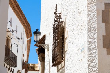 Teslimatçı, güneşli bir günde, İspanya 'da mavi renkli evlerin olduğu dar bir sokakta scooter sürüyor.