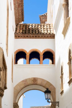 Teslimatçı, güneşli bir günde, İspanya 'da mavi renkli evlerin olduğu dar bir sokakta scooter sürüyor.