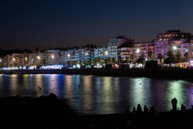 Turistler ve yerliler sahilde bir yaz gecesinin tadını çıkarıyorlar, eğlence gezileri ve canlı müzikle bir festival izliyorlar.