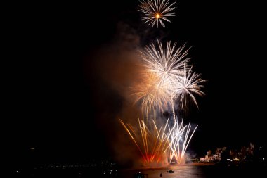 Parlak havai fişekler teknelerin üzerinde patlıyor. Gece gökyüzünü aydınlatıyor.