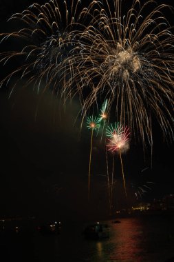 Parlak havai fişekler teknelerin üzerinde patlıyor. Gece gökyüzünü aydınlatıyor.