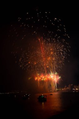 Parlak havai fişekler teknelerin üzerinde patlıyor. Gece gökyüzünü aydınlatıyor.