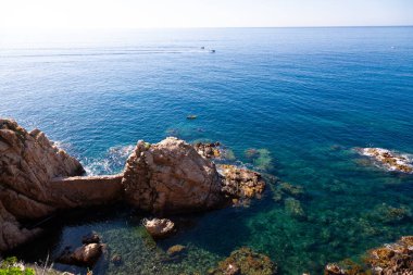 Tekneler güzel turkuaz sularda yüzüyor ve ön planda kayalık kayalıklar var.