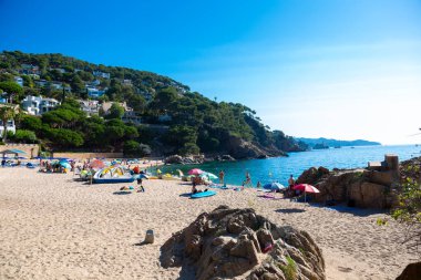 Tourists enjoying the sun and sea on the beautiful beach of aiguablava, located on the stunning costa brava coastline in spain clipart