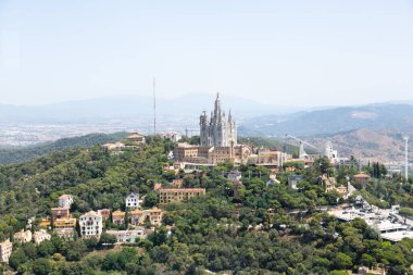 Güneşli bir yaz gününde Barselona şehrine tepeden bakan İsa 'nın kutsal kalbinin vadesi dolmuş kilisesiyle Tibidabo lunaparkının panoramik manzarası.