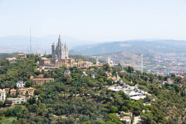 Güneşli bir yaz gününde Barselona şehrine tepeden bakan İsa 'nın kutsal kalbinin vadesi dolmuş kilisesiyle Tibidabo lunaparkının panoramik manzarası.