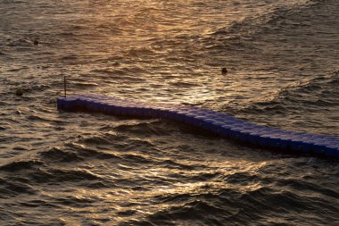 Yumuşak dalgalar altın gün batımını yansıtıyor alacakaranlıkta kumlu bir plajı nazikçe sarıyor.