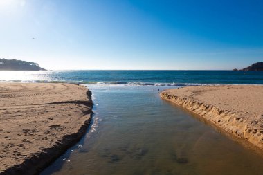 Bulutlu bir günde iki kumlu sahil arasında akan küçük bir deniz suyu deresi.
