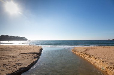 Bulutlu bir günde iki kumlu sahil arasında akan küçük bir deniz suyu deresi.