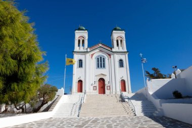 Geleneksel beyaz kilise, kırmızı kapılar, Bizans bayrağı ve derin mavi gökyüzünün altında rüzgarda dalgalanan Yunan bayrağı.