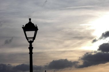 Süslü bir sokak lambası bulutlu bir günbatımı gökyüzünün arka planında dimdik duruyor.