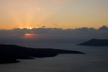 Karanlık bulutların arasından süzülen güneş ışınları huzur dolu bir okyanusun üzerinde nefes kesici altın bir günbatımı yaratır.