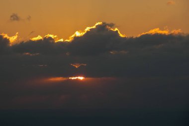 Karanlık bulutların arasından süzülen güneş ışınları huzur dolu bir okyanusun üzerinde nefes kesici altın bir günbatımı yaratır.