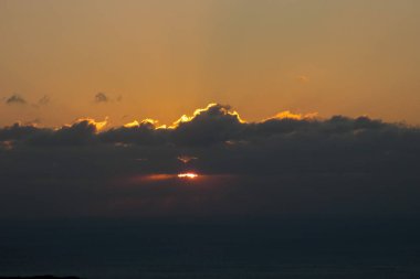 Karanlık bulutların arasından süzülen güneş ışınları huzur dolu bir okyanusun üzerinde nefes kesici altın bir günbatımı yaratır.
