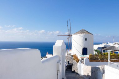 Resimli, bembeyaz, mavi gökyüzüne karşı dimdik duran yel değirmeni geleneksel Yunan mimarisi ve ada cazibesini sergiliyor.