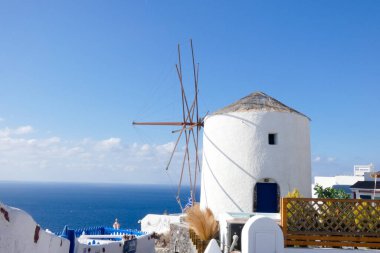 Resimli, bembeyaz, mavi gökyüzüne karşı dimdik duran yel değirmeni geleneksel Yunan mimarisi ve ada cazibesini sergiliyor.