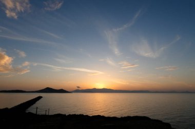 Sokak lambaları, renkli bulutlarla dolu güzel bir günbatımı gökyüzüne karşı siluetler oluşturur.