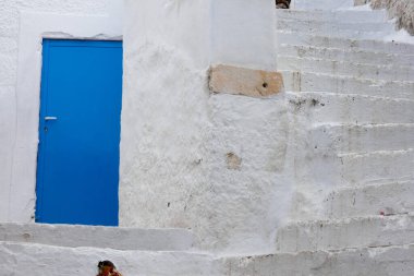 Açık mavi ahşap kapılı oval pencereli ve Yunanistan 'da beyazlatılmış bir evde fener.