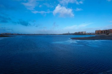 El medano, Tenerlife 'de bulutlu gökyüzünün altında mavi okyanus suyunun kumlu plajla buluşmasının manzarası.