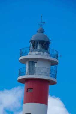 Deniz feneri beyaz bulutlu güzel mavi gökyüzüne doğru yükseliyor.