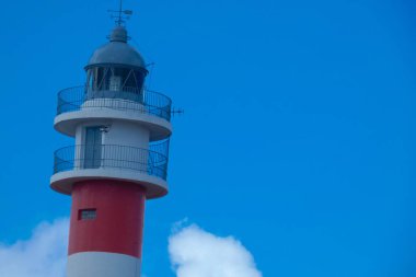 Deniz feneri beyaz bulutlu güzel mavi gökyüzüne doğru yükseliyor.