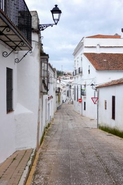 Aracena, Huelva, Endülüs, İspanya 'daki beyaz binalar arasında yokuş yukarı giden dar bir kaldırım taşı caddesi.