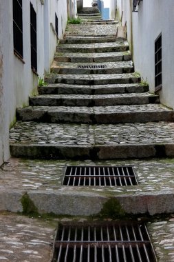 Metal ızgaraları ve beyazlatılmış duvarları olan dik kaldırım taşlı bir sokak. Vejer de la frontera, Cadiz, İspanya 'da yokuş yukarı gidiyor.