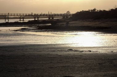 Sakin kıyı manzarası bulutlu bir gökyüzünün altında kumlu bir plajda kıyıya vuran yumuşak dalgaların oluşturduğu sakin bir atmosfer yaratıyor.