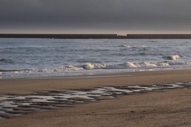 Okyanus dalgaları, bulutlu bir günde dalgalı suların yakınındaki kayalara çarpar ve dramatik bir deniz manzarası yaratır.