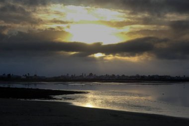 Sahile çarpan okyanus dalgaları üzerinde dramatik kara bulutlarda parlayan güneş ışınları.