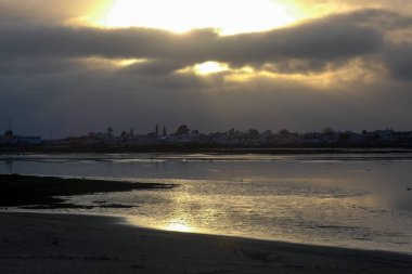 Sahile çarpan okyanus dalgaları üzerinde dramatik kara bulutlarda parlayan güneş ışınları.