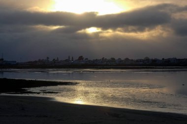 Sahile çarpan okyanus dalgaları üzerinde dramatik kara bulutlarda parlayan güneş ışınları.