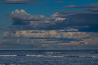 Güzel beyaz kümülüs bulutları, derin mavi bir gökyüzünde görülür. Huzurlu ve manzaralı bir manzara yaratır.